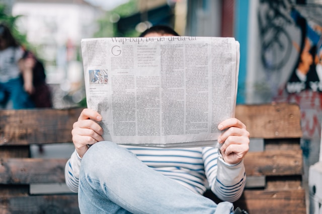 a man reading the newspaper on a bench